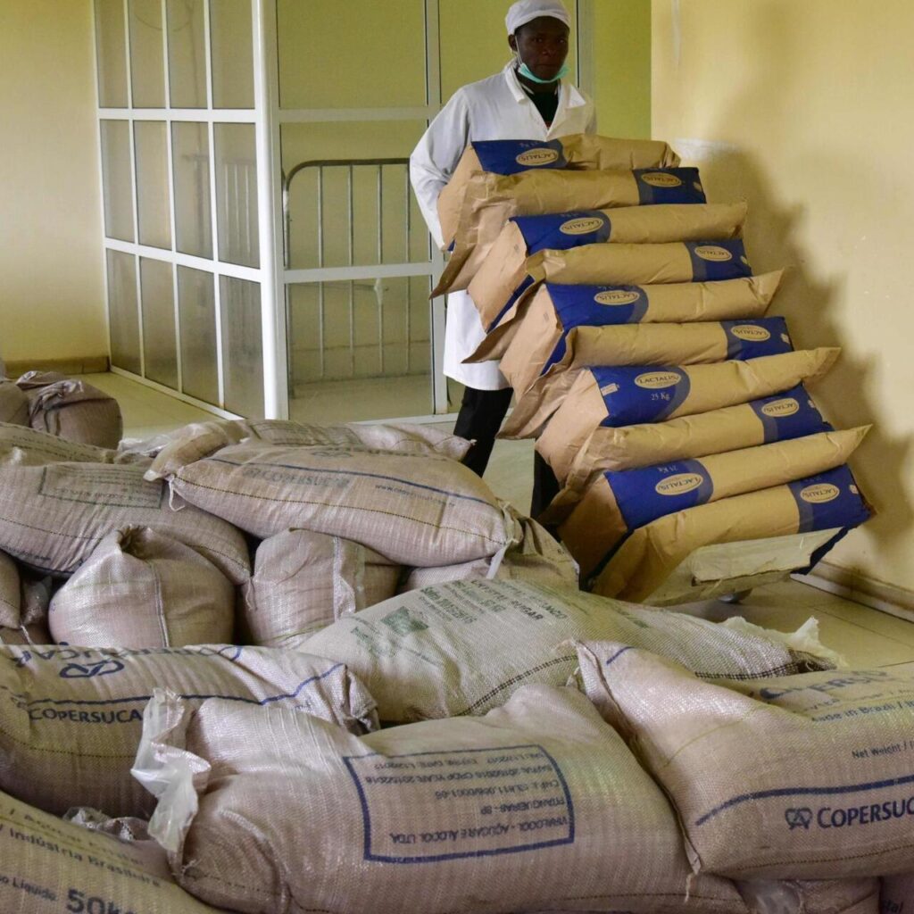 Jeune homme noir portant sur un diable des sacs de lait en poudre de 25kg